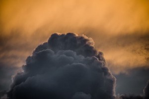 Against a backgrop of orange clouds at sunset a dark grey clouds stands like a dome.