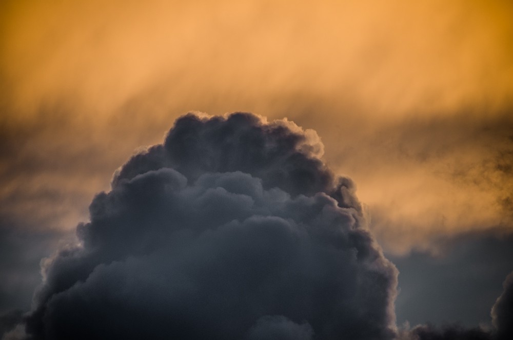 Against a backgrop of orange clouds at sunset a dark grey clouds stands like a dome.