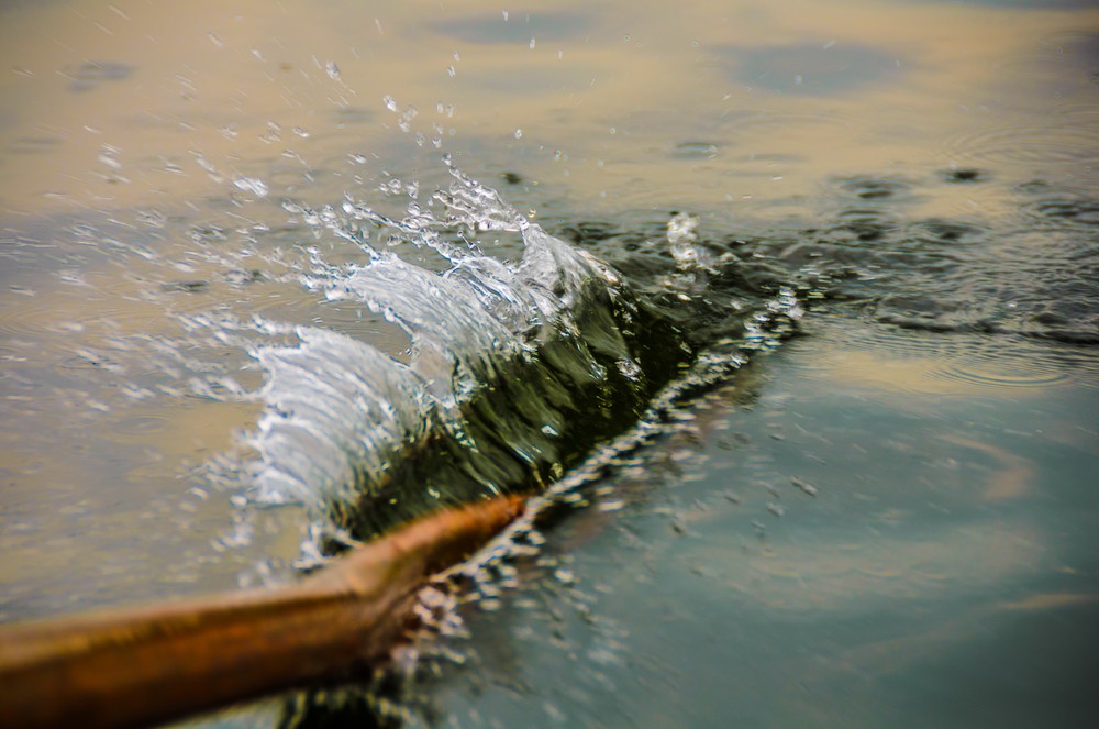 An oar has just been splashed into the water, The splash is in focs while the oar and the rest of the water is slightly blurred.