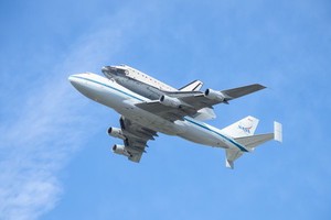 In the blue sky a jumbo jet flies with a space shuttle attached to its back.