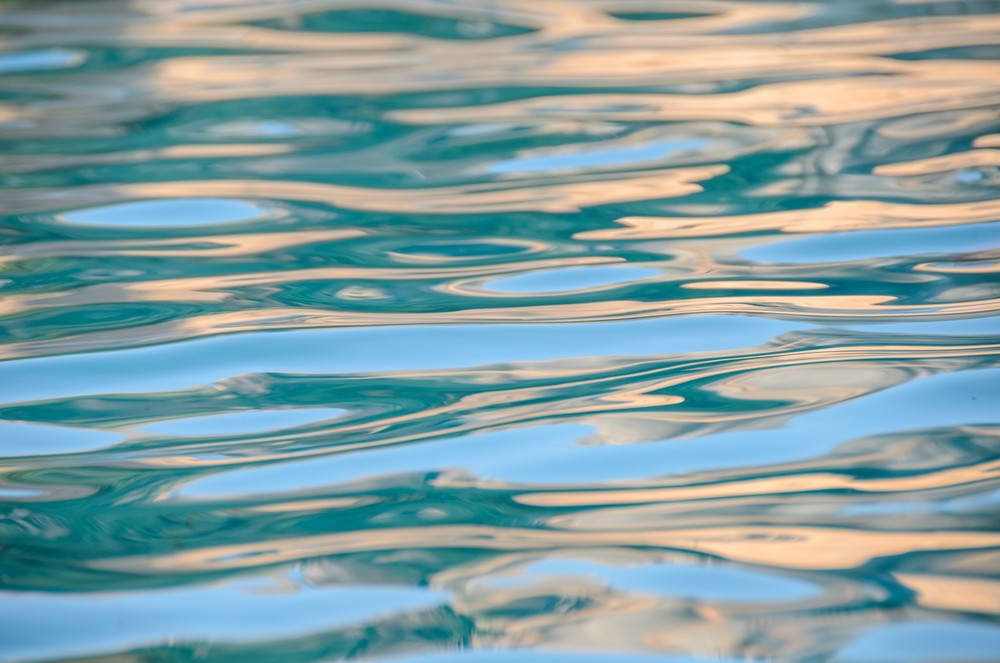 Ripples on the surface of a pool of water show streaks of greens and yellows and blues.