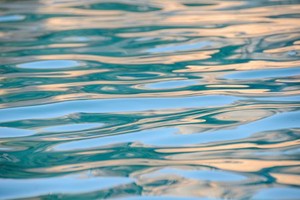 Ripples on the surface of a pool of water show streaks of greens and yellows and blues.